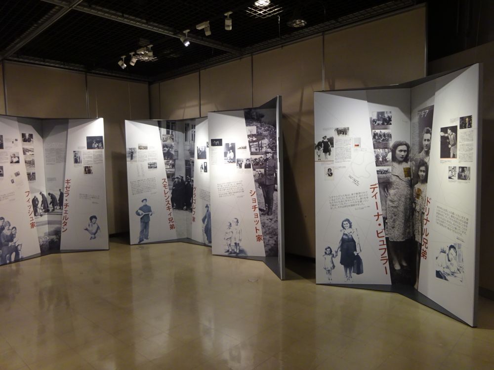 Interior. Four double-winged panels from an L sign, standing under the walls of the room. They consist of collages of black and white photos and writing in Japaneese. The rest of the room is empty.