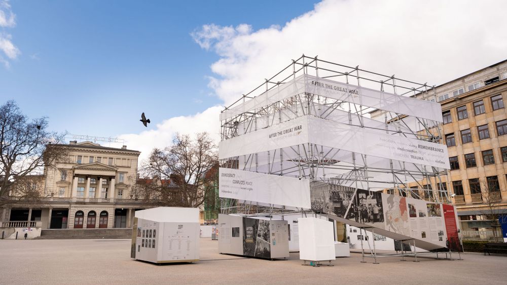 Freedom Square in Poznań. The cube-like installation of After the Great War exhibition stands in the middle of an empty square. On its left, a neoclassical building.