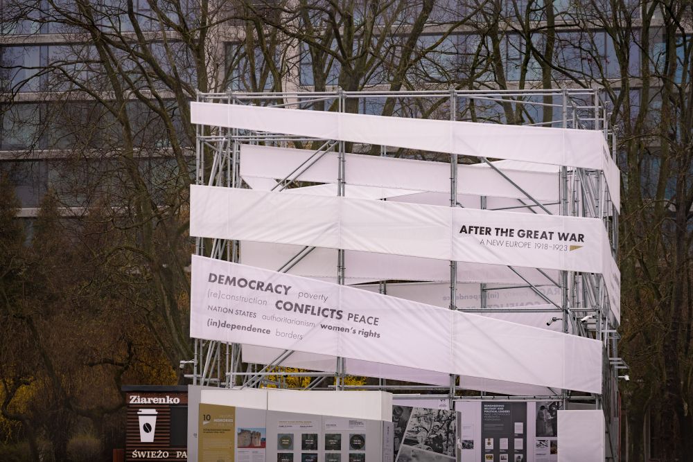 Cloudy day. The photograph centers on the cube-like installation of the After the Great War exhibition. Behind it, in the background, the leafless trees and tall grey builiding.