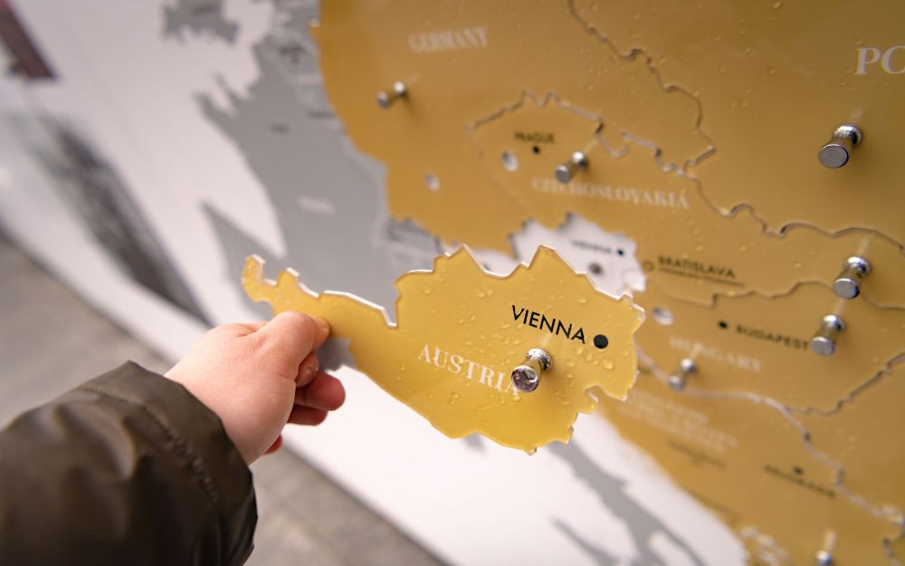 A disembodied hand holds a  yellow cut-out in the shape of the Austrian Republic. It is a part of the larger interactive installation, which allows visitors to compare the pre- and post-war borders of Europe. The rest of the cut-outs is held by the magnets to the inner wall of the After the Great War exhibition.