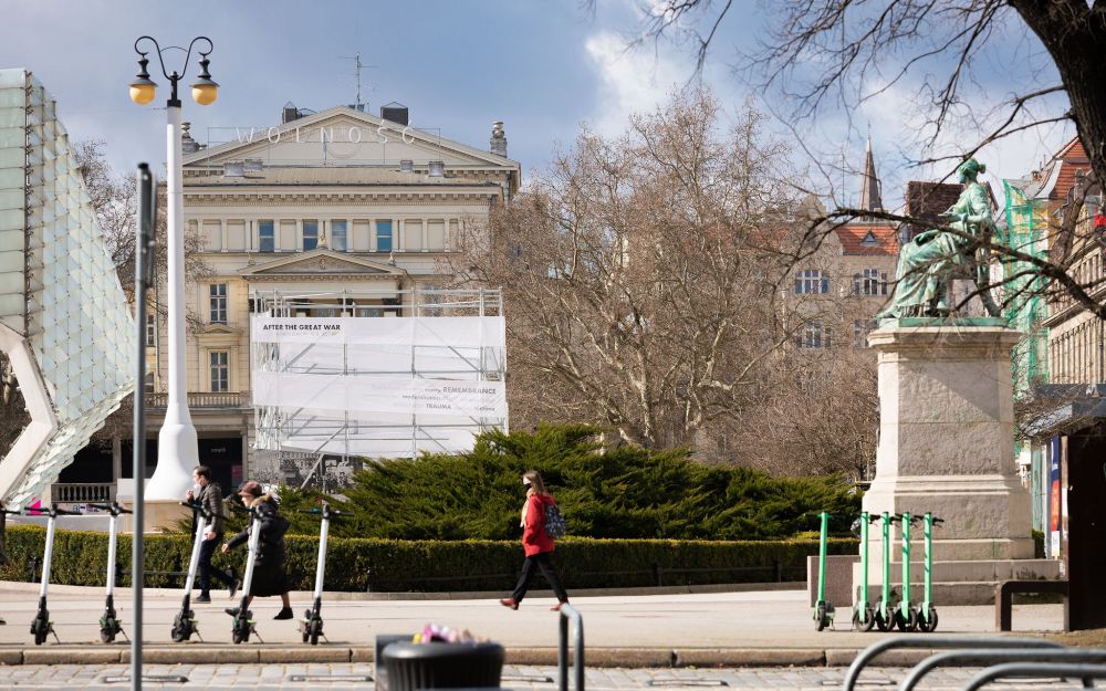 Freedom Square in Poznań. The cube-like installation of the After the Great War exhibition stands on the left, behind the green shrubbery. On the right, the nineteenth-century patine-covered statue of a woman sitting in a chair, representing Hygiene.