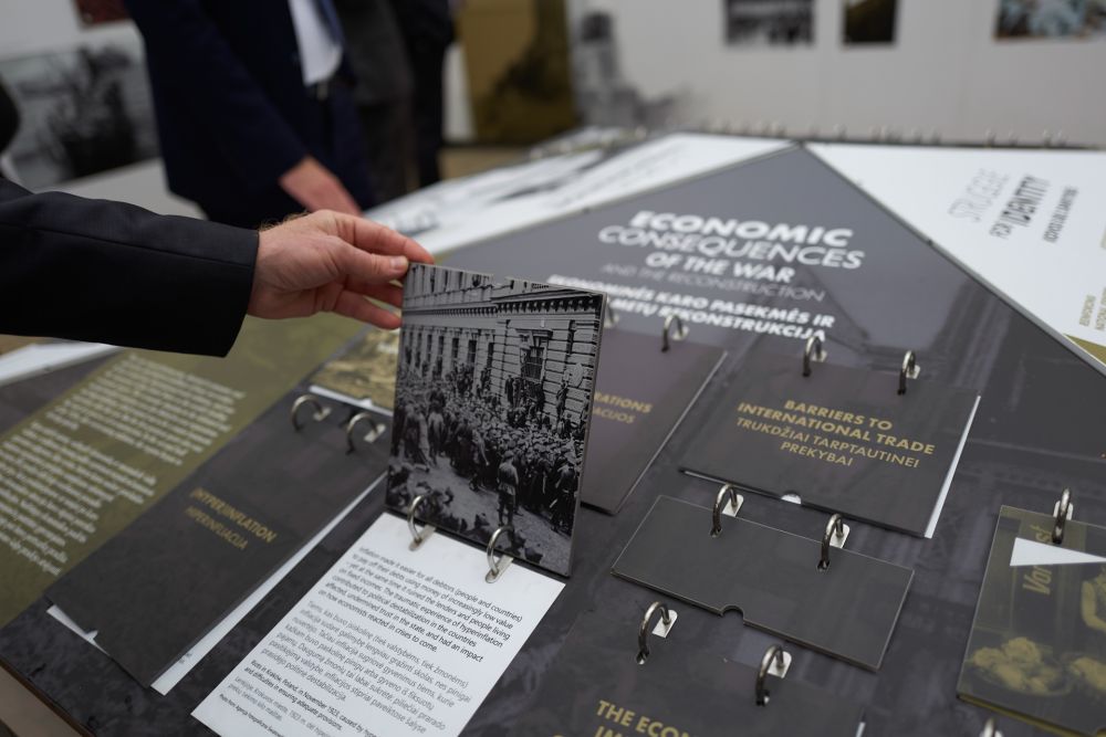 Interior of the installation of After the Great War exhibition. A disembodied hand lifts one of the panels from the central board. It reveals the photography of riot in Kraków, Poland in 1923, and accompanying text on the economic realities of the interwar period.