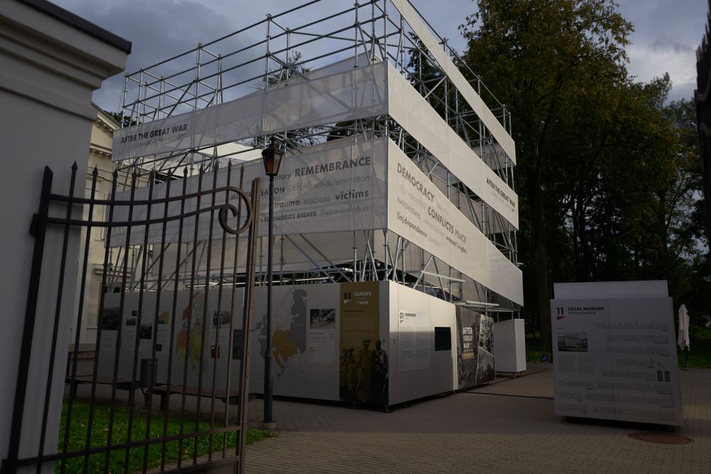 The open neo-classical gate reveals insides of the garden. In the centre of it stands the cube-like installation of After the Great War exhibition. The square in which it stands is empty.