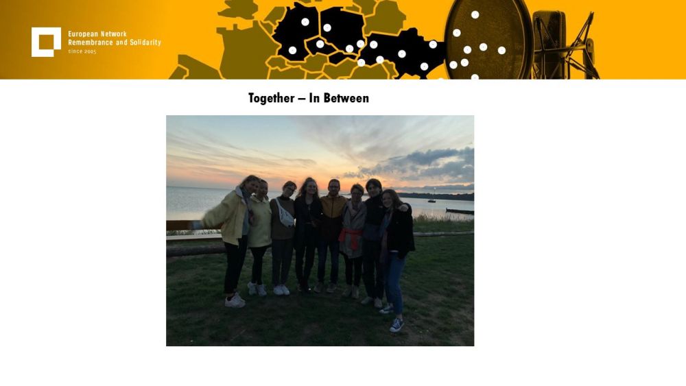 Presentation slide with a single photo on it. It shows a group of seven young people, standing on a beach. Behind them, a body of water and slowly setting-down sun. The group is smiling and holding each other arms. Above all of it, a gold-yellow header with European Network remembrance and Solidarity.