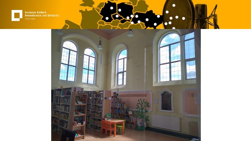 Presentation slide with a single photo in the center. The photo shows an old interior with large windows. Three large bookcases stand against the wall. Next to them, a childrens table and chairs. Above all of it, a gold-yellow header with European Network remembrance and Solidarity.