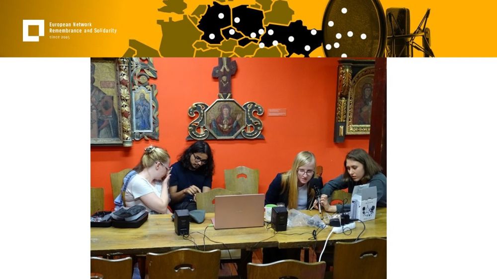 Presentation slide with a single photo in the center. It presents a group of four young people sitting by the table. They are working on setting up audio recording equipment.  Behind them, an orange wall with orthodox icons. Above all of it, a gold-yellow header with European Network remembrance and Solidarity.