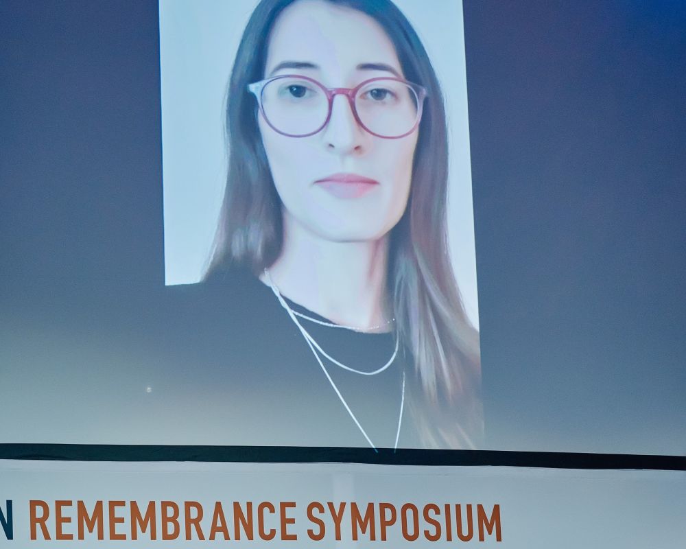 The large screen displays a photo of Maria Axinte, who attends the Ninth European Remembrance Symposium online.