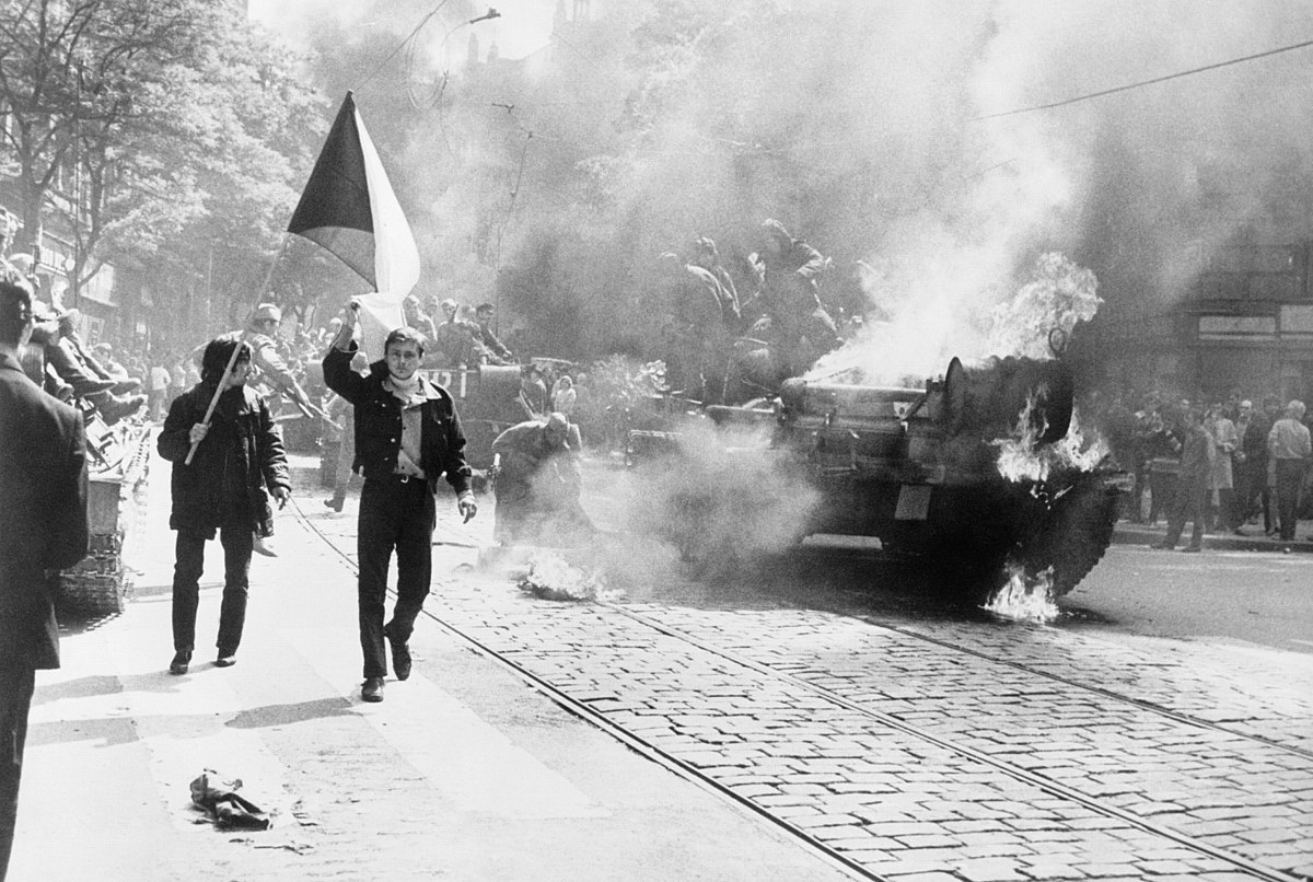 During the Soviet invasion of Czechoslovakia, Czechoslovaks carry their national flag past a burning tank in Prague. Source: CIA  / Public domain