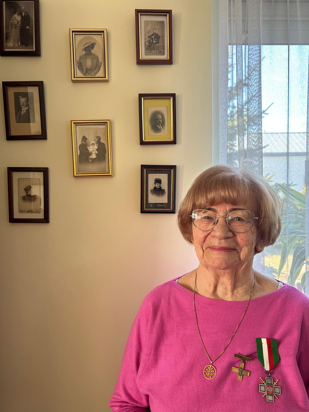 Grandma Basia in front of family photos, wearing her Siberian Exile Cross